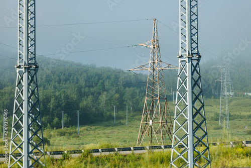 Quadro su tela Transmission towers standing among foggy forest and meadow