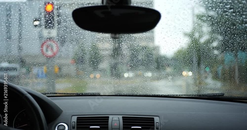 POV car stopped at red traffic light on rainy day with pedestrians crossing street