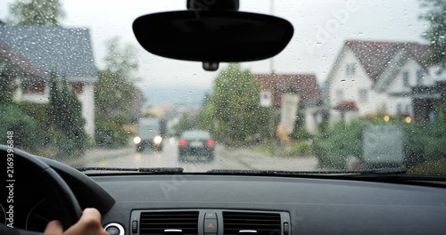 POV car driving on rainy village main road with oncoming traffic through wet windshield