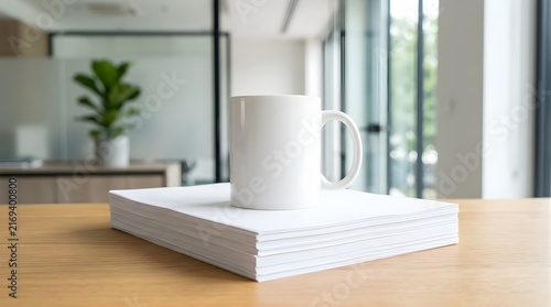 White coffee mug placed on a stack of blank paper on a modern desk
