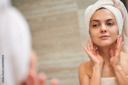 Woman applying skincare, looking at her reflection in mirror