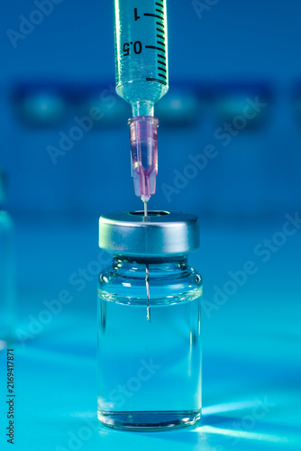 medical syringe with needle next to vaccine medicine glass vials on blue background as a conceptual backdrop for pharmaceutical research healthcare immunization biotechnology and clinical science