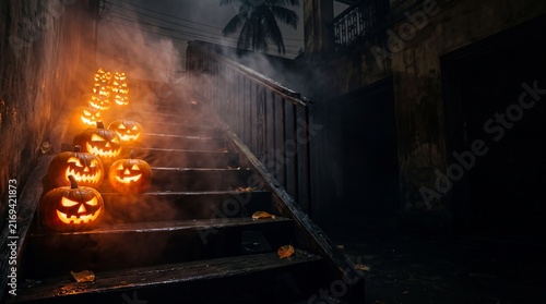 Row of carved glowing jack lanterns lined up on dark old wooden staircase covered in dense smoke at night for spooky halloween backyard