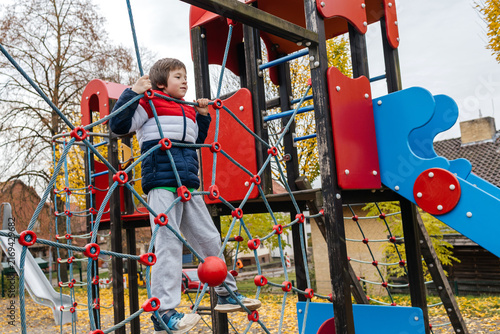 Child boy climbing rope net at playground in autumn