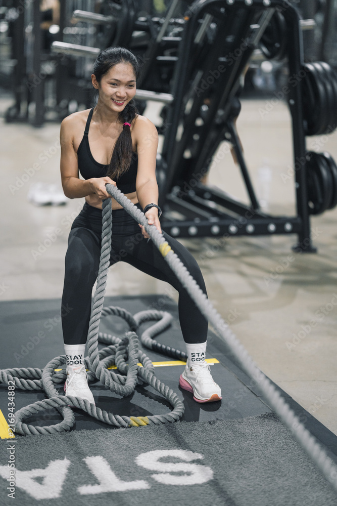 Naklejka premium Woman exercising with battle ropes or training sled pull in gym