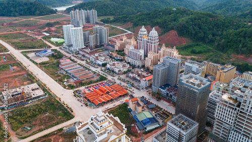 Aerial view of the developing border town of Boten with modern high-rise buildings, construction sites, and a central market area surrounded by hills in Boten, Sainyabuli Province, Laos.