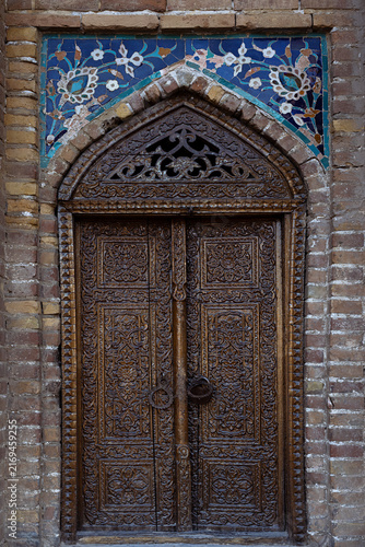 Obraz na płótnie Carved wooden door of Gur-e-Amir mausoleum in Samarkand with intricate floral patterns and blue mosaic tilework above