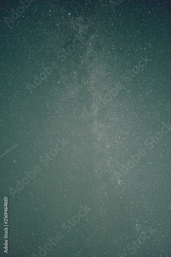 Vertical night sky shows bright Milky Way band, scattered stars, subtle meteor streak, deep dark horizon, soft grain texture, upward view with calm cosmic atmosphere for astronomy, space, science