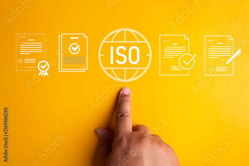 Finger pointing at ISO standard globe symbol surrounded by certified document and contract icons on bright yellow background