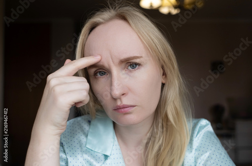 A adult woman touching forehead wrinkle between eyebrows and looking in mirror. She is concerned about aging lines, frown lines, facial skin care, and botox injections.