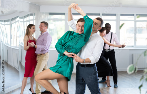 Obraz na płótnie Happy man and woman in elegant clothes performing ballroom dance in dancing room