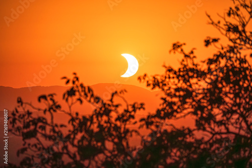 Obraz na płótnie The setting sun with parial solar eclipse over the forest, taken on Lindenplatz,  Loerrach, Germany on 12