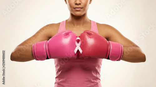 Female boxer in pink gloves and breast cancer awareness ribbon in a firm fighting stance, showing strength, hope, courage, resilience, empowerment, support, care and breast cancer awareness
