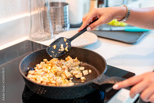 Fotografía Woman cooking chicken and onions in kitchen pan