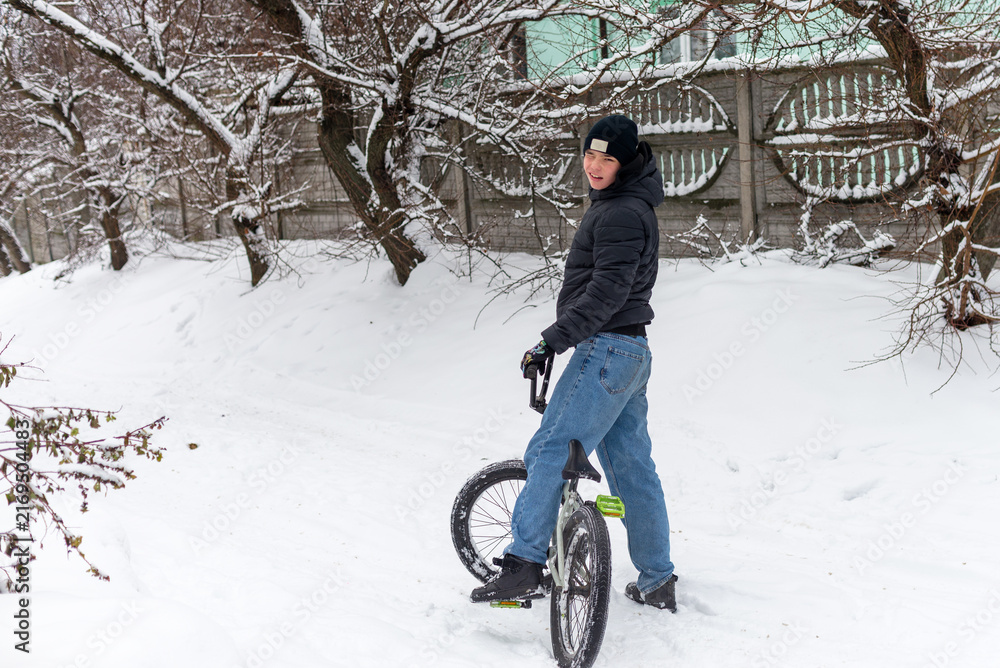Naklejka premium Teenager boy riding a BMX bicycle in a snowy winter park or backyard