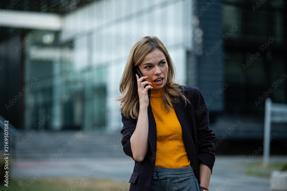 Fototapeta premium Businesswoman talking on smartphone outside office building