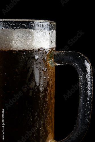 Frothy beer mug sits on dark surface with condensation forming on glass during evening gathering