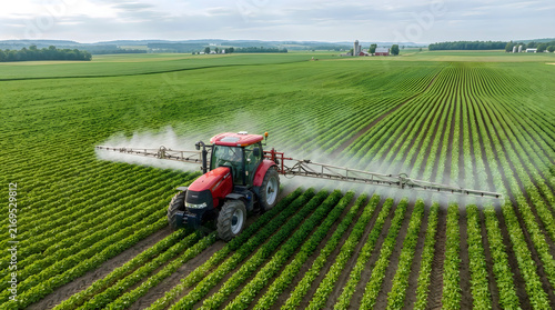 Red tractor spraying crops in a green field isolated on white background