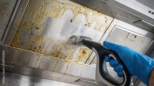 Professional steam cleaner removing built-up grease from a stainless steel kitchen range hood, representing deep cleaning, sanitation, maintenance and household hygiene