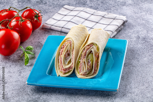 Фотография Wrap sandwich with ham cheese and lettuce on blue plate with fresh tomatoes