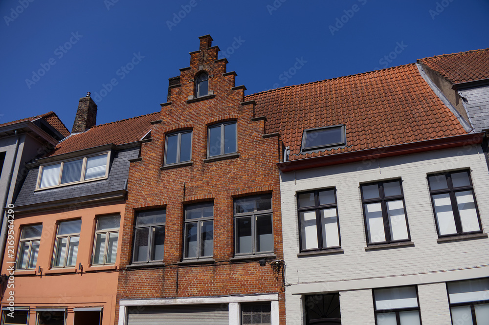 Fototapeta premium Historic European red brick house with a traditional stepped gable roof against a clear blue sky. Typical Flemish or Dutch urban real estate architecture.