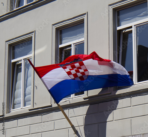 Bild auf Leinwand Waving national flag of Croatia hanging from a building window against a gray facade