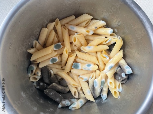 Cooked penne pasta in a metal container is heavily contaminated with gray-green, white fuzzy mold.