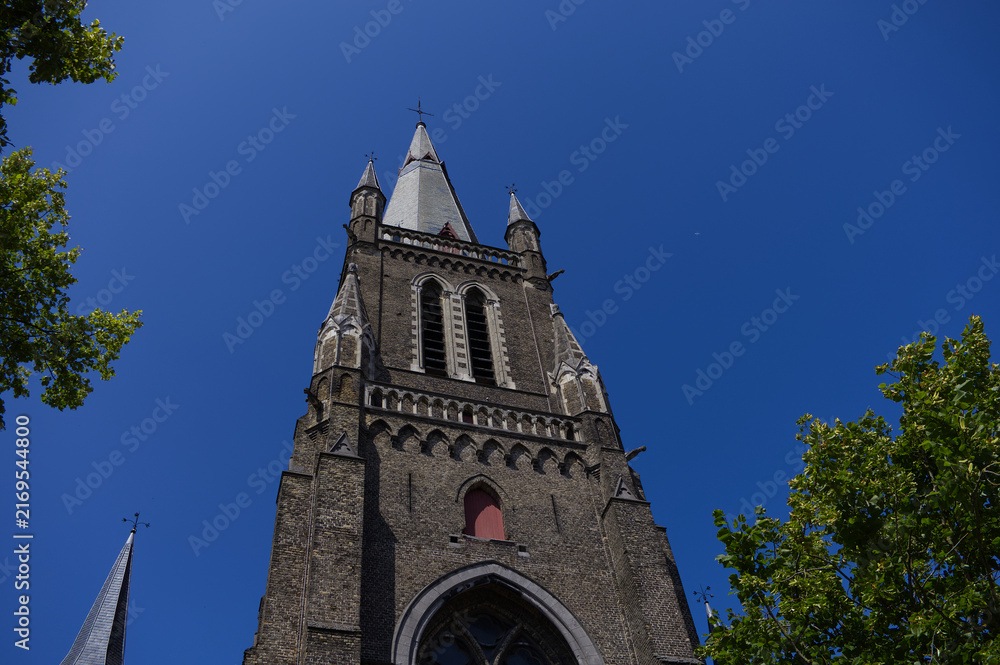 Fototapeta premium Imposing gothic brick church tower with arched windows and pointed spires against a clear blue sky. Historic medieval European religious architecture.
