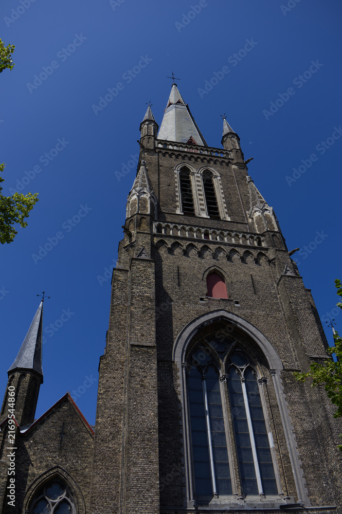 Fototapeta premium Imposing gothic brick church tower with arched windows and pointed spires against a clear blue sky. Historic medieval European religious architecture.