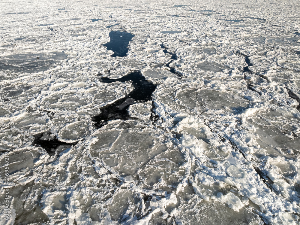 Fototapeta premium Traffic-filled bridge spanning a river filled with drifting ice floes.