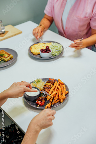 Bild auf Leinwand Two diners eat plated meals at a white restaurant table, including grilled meat
