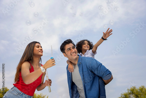 Happy parent with their son having fun with flying bubbles in the park