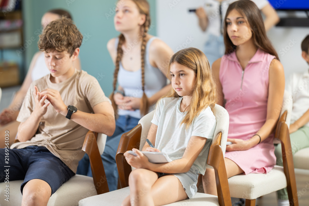 Obraz premium Attentive children and teenagers listening to teacher on chairs inside modern classroom interior