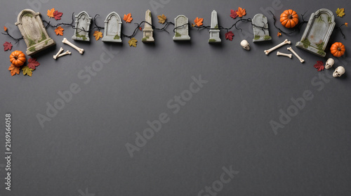 Halloween flat lay background with miniature tombstones, pumpkins, and bones on dark grey
