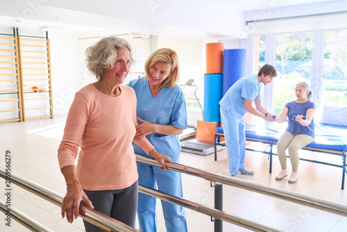 Senior Woman Walking With Parallel Bars Assisted By Physiotherapist In Rehab Center For Rehabilitation And Recovery After Injury Indoors