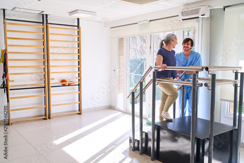 Senior Woman Doing Stair Climbing Exercise With Physiotherapist Assistance In Rehab Center For Injury Recovery And Rehabilitation Program Indoors