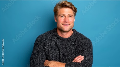A confident man with crossed arms smiles warmly against a blue background.