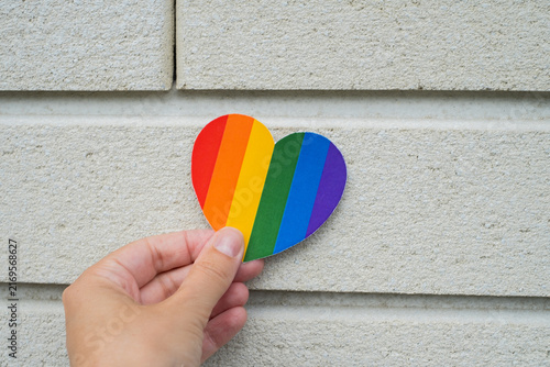 Canvastavla Hand holding rainbow heart symbol on light wall background for LGBTQ pride and e