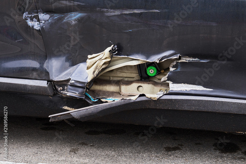 Close-up of a damaged car door with large torn opening after a traffic accident. Deformed metal and exposed internal components