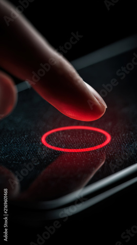 Finger touches red circle on smartphone screen at night to perform action or unlock device with biometric sensor