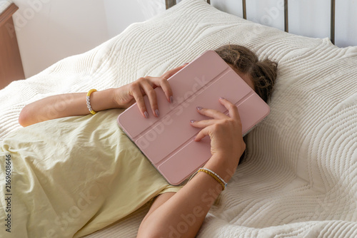 Obraz na płótnie teenage girl lying in bed, covering her face with a digital tablet