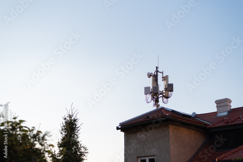Telecommunications cellular antenna mounted on the tiled roof of residential building against blue sunset sky