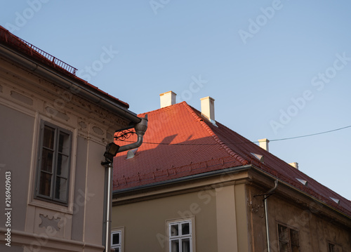 Historic European buildings feature red tiled roofs and white chimneys against clear blue sky. Petrovaradin, Serbia