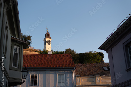 Historic clock tower rising above traditional red-tiled rooftops against clear blue sky