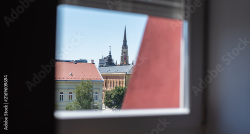 View through window to Novi Sad city centre with tiled roofs and distant Name of Mary Church spire