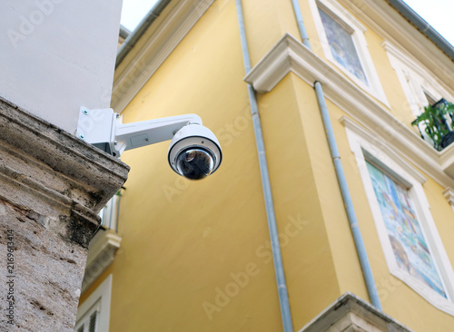 White modern cctv security camera mounted on stone wall of historical yellow building. Great concept for urban surveillance article, public safety presentation or property protection system banner