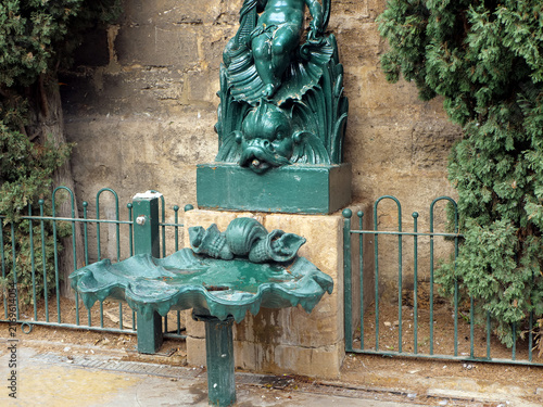 Vintage green metal drinking fountain with shell basin and cherub sculpture in park. Perfect backdrop for classic European landscaping catalogs, historic park architecture articles or travel guides