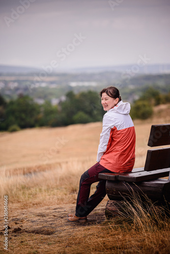 Canvas Print Happy female traveler sitting on outdoor wooden bench turning back to smile during autumn hike in nature
