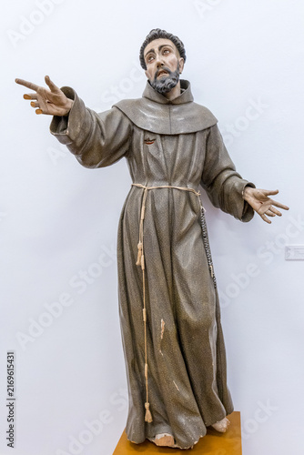 A wooden statue of a Franciscan monk with open arms