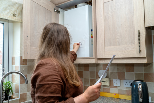 Woman adjusting home boiler while checking heating and energy costs